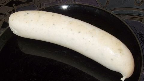 Eine große, hellweiße Weißwurst liegt auf einem schwarzen Teller und hebt den traditionellen bayerischen Genuss hervor.