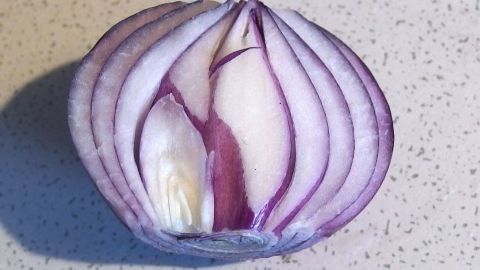 Saft einer Zwiebel desinfiziert die Haut und beseitigt Rötungen. Eine rote Zwiebel ist halbiert und zeigt ihre innenliegenden Schichten auf einer hellen Arbeitsfläche, ideal gegen Pickel.