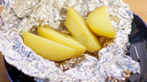 Leckere Pellkartoffeln mit Frittensalz / Pommesgewürz und Olivenöl. Pellkartoffeln liegen auf Alufolie in einer Schüssel, bereit, mit Frittensalz und Olivenöl serviert zu werden.