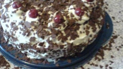 Eine üppige Schwarzwälder Kirschtorte mit Sahne, Schokoladenraspeln und Kirschen wird auf einem Tisch serviert.