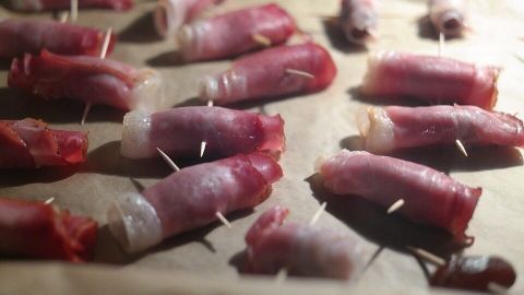 Schinkenröllchen mit Frischkäse liegen auf Backpapier, fixiert mit Zahnstocher, bereit zum Backen oder Servieren.