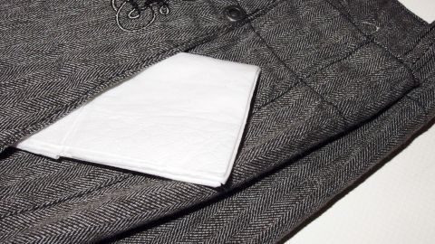 Papiertaschentuch mitgewaschen und und die Klamotten sind voller Fussel? Ab in den Trockner damit und die Wäsche ist wieder fusselfrei. Ein Papiertaschentuch liegt auf grauen Stoffhosen, bereit, Fusseln zu entfernen, möglicherweise nach dem Trocknen.