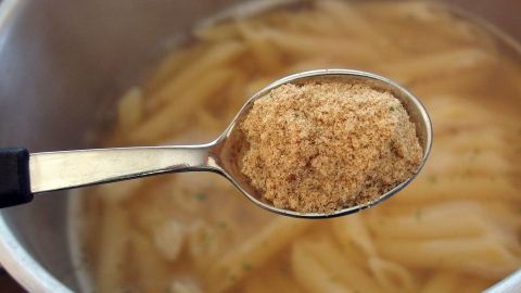 Ein Löffel mit Brühe wird über einen Topf Nudeln gehalten, die in heißem Wasser kochen.