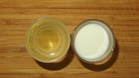 Zwei Schalen mit Milch und Öl liegen nebeneinander auf einem Holzbrett, bereit zum Mischen für den Dip.