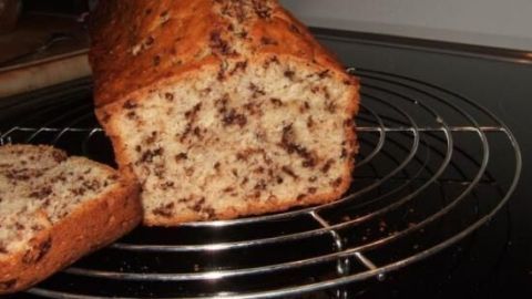 Bananenbrot mit Schokostückchen steht teilweise angeschnitten auf einem Gitter zum Abkühlen in einer Küche.