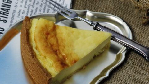 Ein Stück Käsekuchen eifrei liegt auf einem silbernen Teller, umgeben von rustikalem Tischzeug und einer Zeitung.