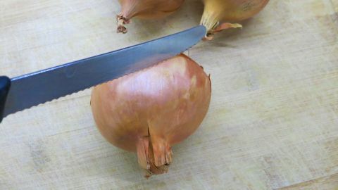 Eine Zwiebel liegt auf einem Holzbrett, während ein Messer sie schneidet, um zur Zubereitung von Speisen vorbereitet zu werden.