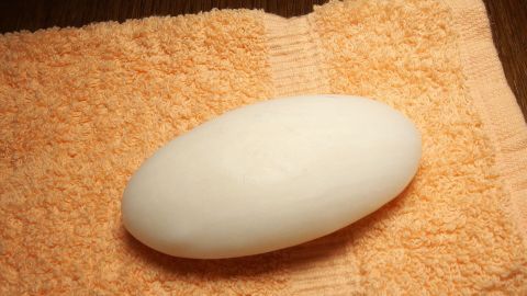Ein weißer Seifenstein liegt auf einem orangefarbenen Handtuch, ideal für die Gesichtswäsche bei Pickeln und Akne.