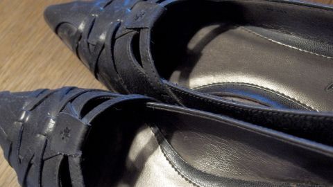 Drückende Schuhe mit heißem Wasser ausspülen und mit Socken anziehen - tragen, bist die Schuhe trocken sind. Schwarze, spitze Schuhe liegen auf einem Tisch, bereit, mit heißem Wasser geweitet zu werden.