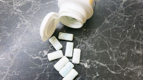 Kaugummistücke liegen verstreut auf einer marmorierten Oberfläche, während eine geöffnete Flasche daneben steht.