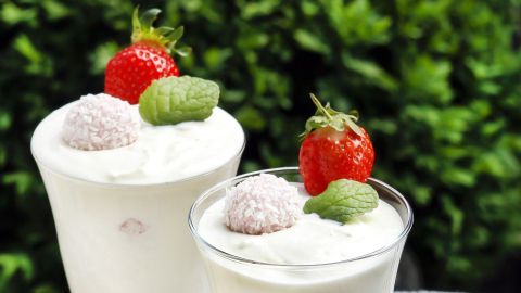 Zwei elegante Gläser mit Raffaello-Creme stehen auf einem gemusterten Tischset, umgeben von frischen Erdbeeren und Minzblättern.