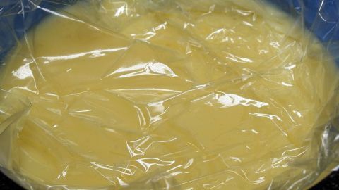 Ein Pudding ohne Haut ruht in einer Schüssel, abgedeckt mit Frischhaltefolie, bereit zum Abkühlen.
