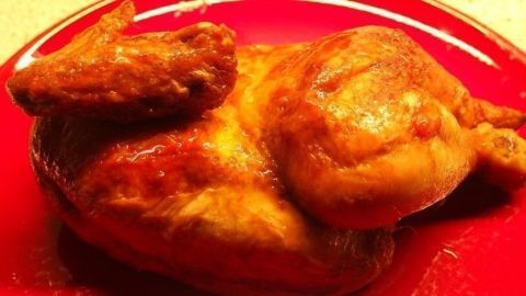 Ein gebratenes Hähnchen liegt auf einem roten Teller, außen knusprig und appetitlich, innen saftig und frisch.