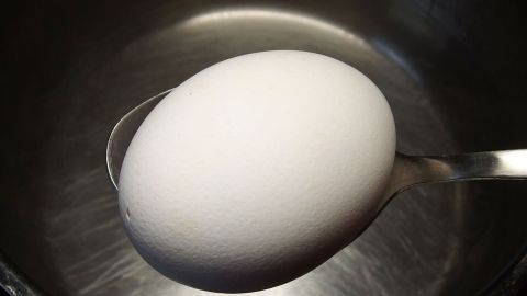 Ein Ei wird vorsichtig mit einem Löffel ins Wasser gelegt, um energiesparend Eier zu kochen.