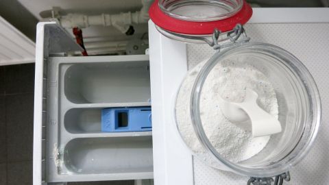 Ein Waschmaschinenfach mit einem lila Einleger und einem offenen Glas mit Waschpulver daneben, bereit zum Befüllen.