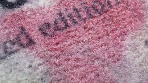 Ein Fleck aus Rotwein ist auf einem Textil sichtbar, wobei der Hintergrund unscharf und strukturiert ist.
