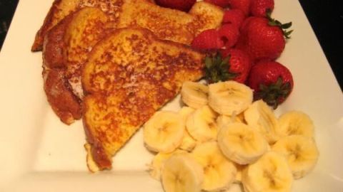 French Toast auf weißem Teller, serviert mit frischen Erdbeeren, Himbeeren und Bananenscheiben; appetitlich angerichtet.