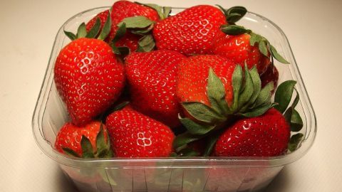Eine transparente Schale mit frischen Erdbeeren steht auf einem Tisch und zeigt die saftigen, roten Früchte.