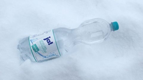 Eine Wasserflasche liegt in frischem Schnee und verdeutlicht, wie man Strom sparen im Kühlschrank im Winter kann.