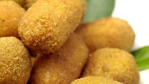 Knusprige, goldbraune Suppli romani liegen gestapelt auf grünen Blättern, die essbare Reiskroketten betonen.