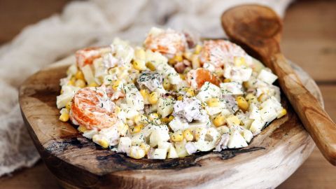 Der Salat besteht aus Mais und Thunfisch, serviert in einer rustikalen Holzschüssel auf einem Holztisch.