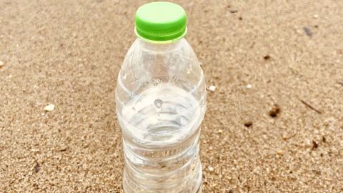 Eine Plastikflasche mit Wasser steht im Sand, während die Wellen sanft den Strand erreichen, ideal für kühle Getränke am Strand.
