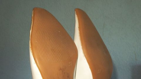 Zwei glatte Schuhsohlen stehen aufrecht vor einer einfarbigen Wand, die den minimalistischen Stil betont.
