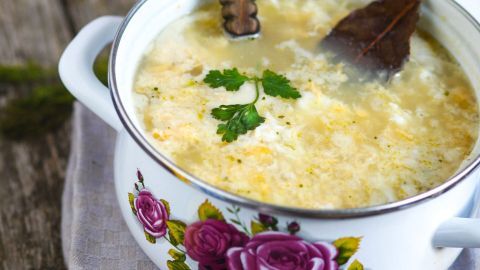 Eine Schale mit saurer Eier-Suppe steht auf einem rustikalen Holztisch, während ein Löffel im klaren, aromatischen Brühe rührt.