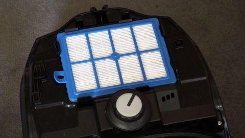 Ein blauer Staubsaugerfilter liegt auf dem Staubsauger. Er wird auf seine Sauberkeit überprüft, um gewaschen zu werden.