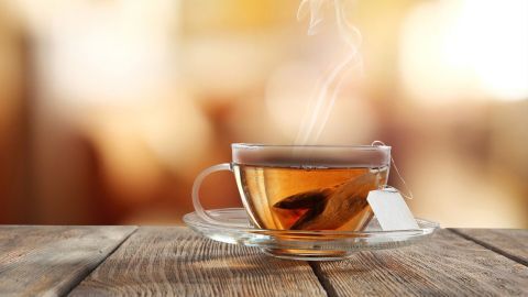 Eine dampfende Tasse Tee steht auf einem Holztisch, während die gemütliche Umgebung eine entspannende Atmosphäre schafft.