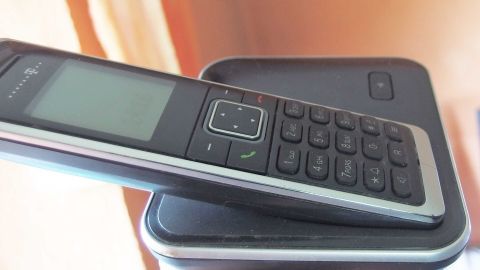 Ein Telefon liegt auf einer Basisstation, während unerwünschte Werbeanrufe im Hintergrund vermieden werden sollen.