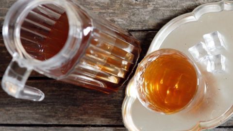 Gesunder Durstlöscher für heiße Sommertage mithilfe von Tee (egal welche Sorte, am besten Schwarztee), Orangensaft und Mineralwasser. Ein klarer Krug und ein Glas mit einem gesunden Getränk stehen auf einem rustikalen Holztisch und strahlen Frische aus.