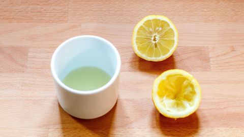 Eine halbe Zitrone und ein Becher mit Zitronensaft stehen auf einem Holztisch, bereit zur Anwendung gegen Obstfliegen.
