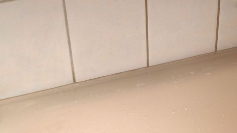 Schwarzer Schimmel ist auf Silikon-Fugen sichtbar, die sich entlang der Fliesen in einem Badezimmer befinden.
