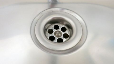 Ein Abfluss in einer Edelstahlspüle zeigt Löcher, durch die Wasser abfließt, während ein unangenehmer Geruch entstehen kann.