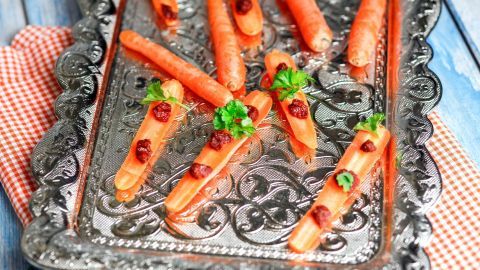Ein toller und gesunder Snack für zwischendurch: Möhre halbieren und mit Tomatenmark-Tupfern verzieren. Fertig sind die süßen Möhrenschiffchen. Auf einem silbernen Tablett liegen kunstvoll dekorierte Möhren-Schiffchen, gefüllt mit kleinen Beeren und garniert mit Kräutern.