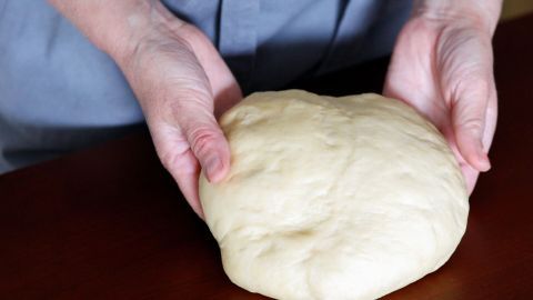 Ein weicher Quark-Ölteig wird von zwei Händen gehalten und auf einer Holzfläche vorbereitet.