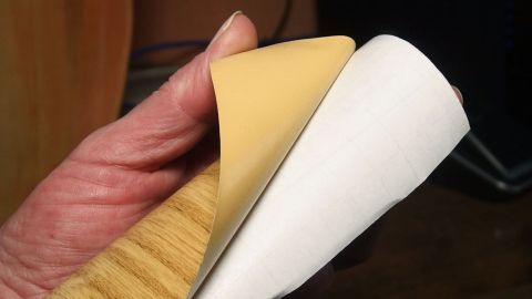 Eine Hand hält selbstklebende Folie, während sie sie vorsichtig abzieht, um Blasenbildung zu vermeiden.