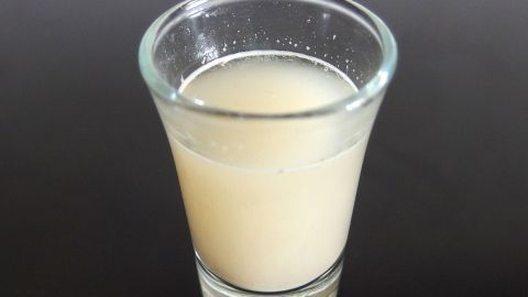 Ein klarer Shot-Glas mit einer trüben Flüssigkeit darin steht auf einer dunklen Oberfläche, während Mückenstiche mit Bierhefe verhindert werden sollen.