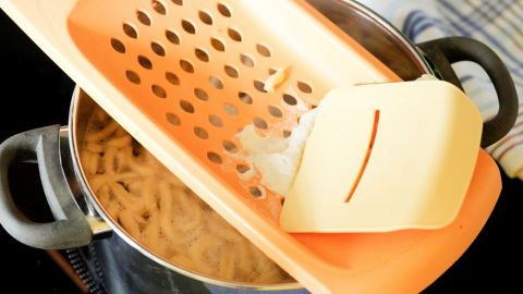 Ein Spätzlehobel wird über einem Topf mit kochendem Wasser gehalten, um die frischen Spätzle gleichmäßig zu portionieren.