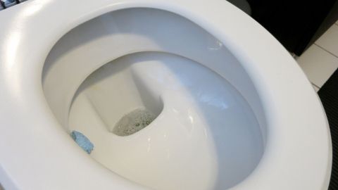 Mit ca. 200 ml Essigessenz bekommt man einen verschmutzten Toilettenabfluss wieder sauber. Eine weiße Toilette steht im Badezimmer, das Wasser im Abfluss zeigt Anzeichen von Verschmutzung und Ablagerungen.