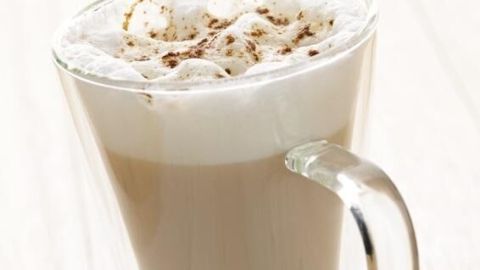 Ein Glas Chai-Tea-Latte mit cremigem Milchschaum und Zimt darauf steht auf einem hellen Tisch.