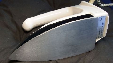 Sämtliche Verschmutzungen am Bügeleisen einfach beseitigen mit einem alten Lappen und etwas Glaskeramikfeldreiniger. Ein Bügeleisen liegt auf einem weichen Untergrund, bereit zum Reinigen mit Glaskeramikfeldreiniger, um Schmutz zu entfernen.