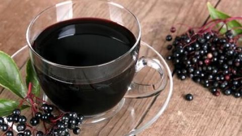 Eine Tasse Holundersaft steht auf einem Holztisch, umgeben von frischen Holunderbeeren und grünen Blättern.