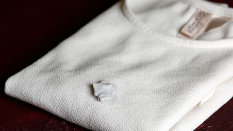 Kaugummi in Kleidung aus Polyester mithilfe von Gallseife und warmem Wasser mühelos entfernen. Ein weißes Polyester-T-Shirt liegt ordentlich gefaltet auf einem Tisch, mit einem Kaugummi, der daran klebt.