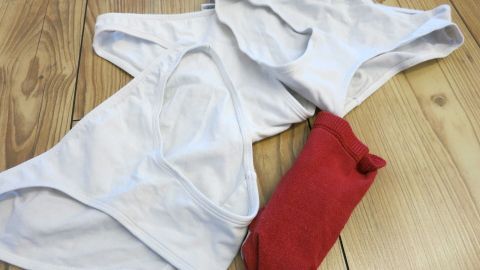 Weiße Unterhosen liegen auf einem Holzfußboden, zusammen mit einer roten Socke, bereit zum Waschen.