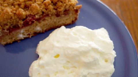 Ein Stück Kuchen mit Streuseln liegt auf einem Teller, daneben befindet sich ein Klecks Sahne, alles appetitlich angerichtet.