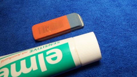 Kugelschreiberfleck aus weißer Hose entfernen mit Zahnpasta und Radierer. Ein Radierer und eine Zahnpasta liegen auf einem blauen Untergrund nebeneinander, bereit, Kugelschreiberflecken zu entfernen.