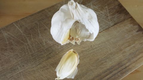 Flöhe bei Haustieren ganz einfach loswerden mithilfe von Knoblauch. Eine Knoblauchzehe liegt auf einem Holzbrett, umgeben von einer Knoblauchknolle, die bereit ist, gegen Flöhe eingesetzt zu werden.