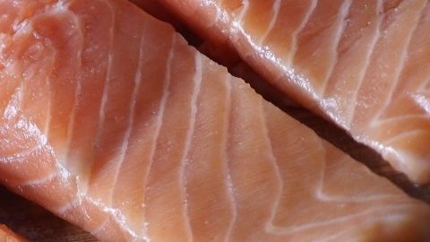 Zwei Stücke geräucherter Lachs liegen nebeneinander auf einer Holzoberfläche, bereit zur Verkostung oder Zubereitung.